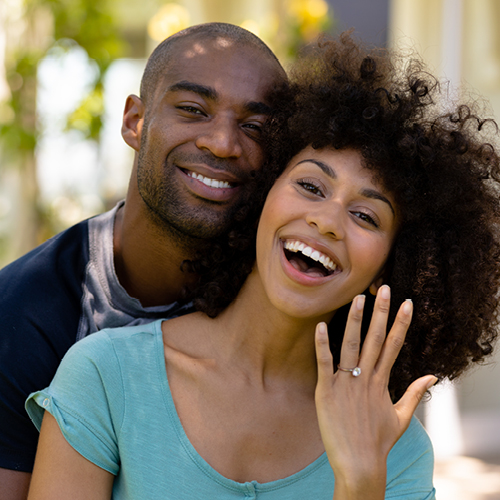 Smiling young, newly engaged couple, showing off ring.