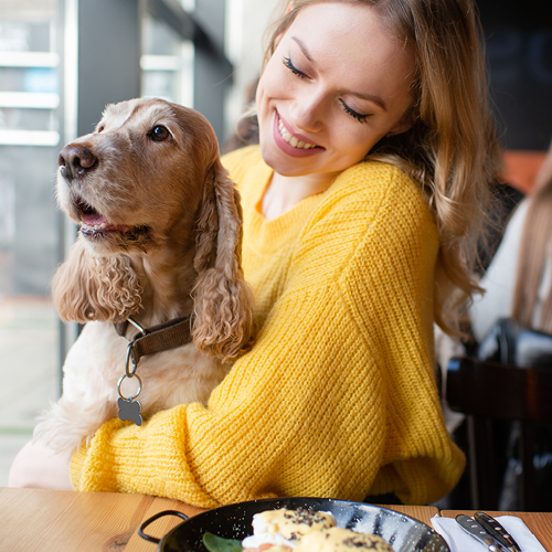 Young woman sitting at table, petting and hugging golden retriever dog.